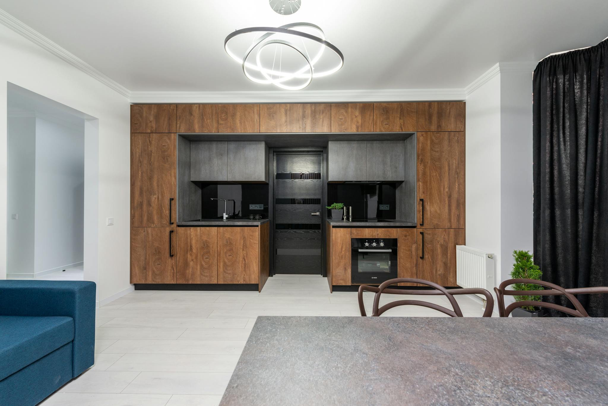 Creative design of kitchen with cupboards and built in oven against table and sofa in house with geometric lamp